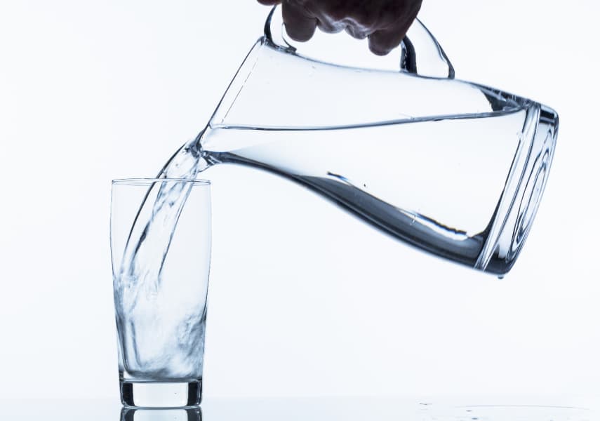 person pouring water from a glass pitcher into a glass